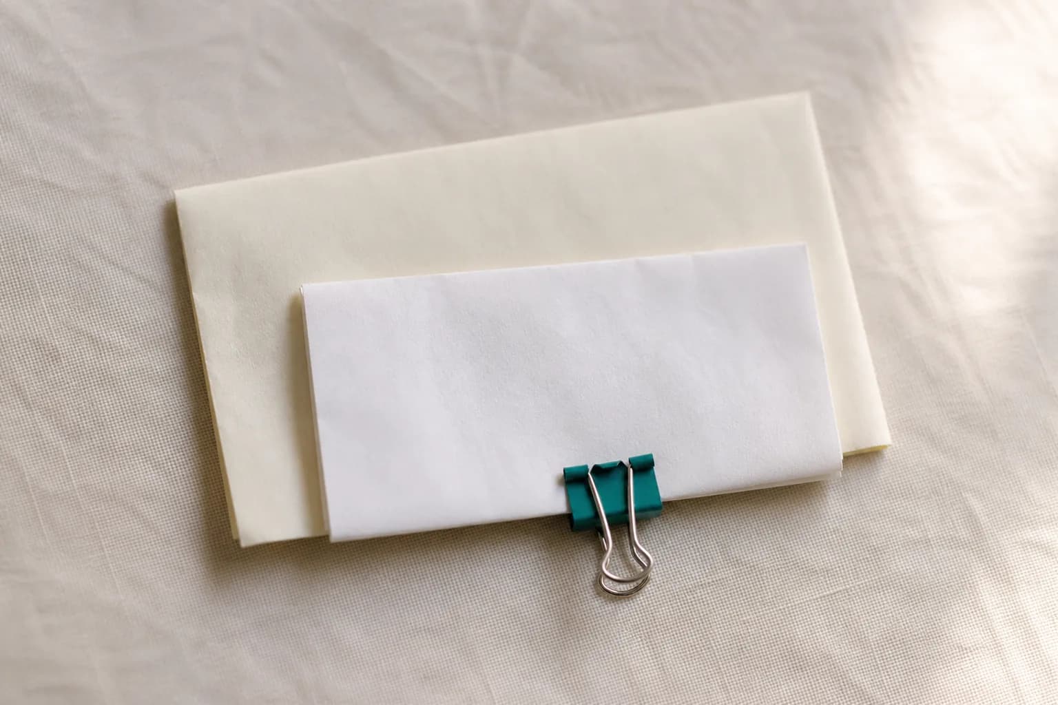 Two blank envelopes of different sizes held together with a small teal binder clip